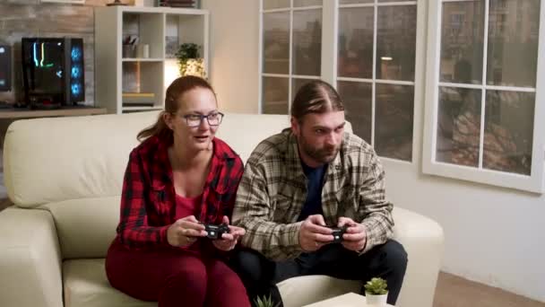 Man and woman sitting on sofa playing video games — Stock Video