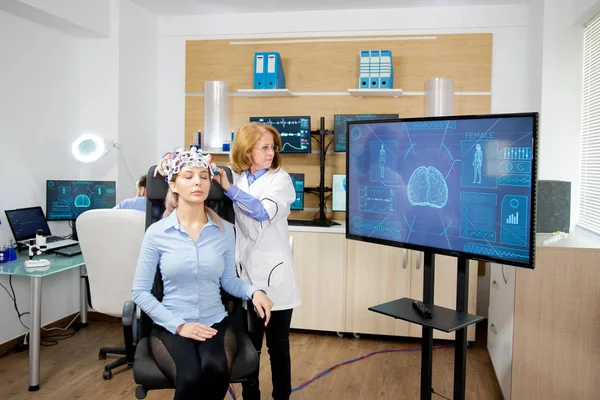 Doctor tracking the data transmitted by the brainwaves scanning headset on a large monitor — 스톡 사진