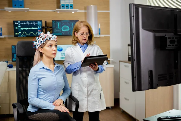 病人妇女扫描她的大脑，医生在平板电脑上做笔记，手里拿着它 — 图库照片