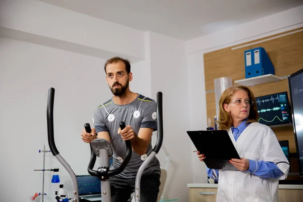 Atleta masculino que hace un esfuerzo físico en el escalón y tiene electrodos conectados a él y al médico que sigue su evolución en la pantalla —  Fotos de Stock