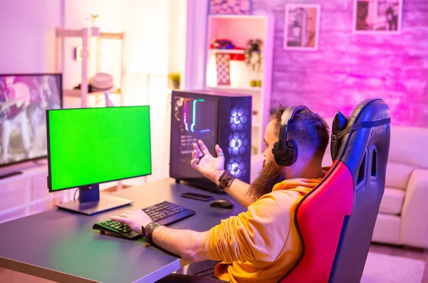 Homem jogando no PC de jogos powerfull em uma sala com luzes de néon em um computador de tela verde — Fotografia de Stock