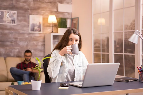 Namorada desfrutando de uma xícara de café enquanto trabalhava no laptop de casa — Fotografia de Stock