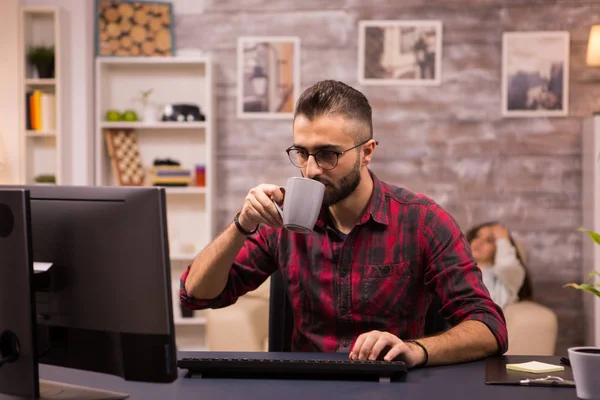 白人企业家在家里的电脑上工作时喝了一小口咖啡 — 图库照片