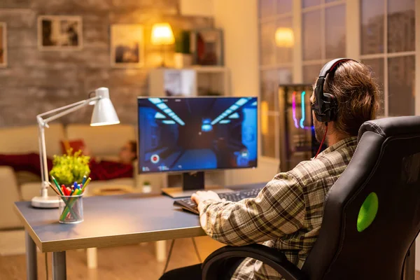 Vista posterior de jugador masculino jugando un tirador en su computadora de gran alcance de la PC tarde en la noche en la sala de estar —  Fotos de Stock