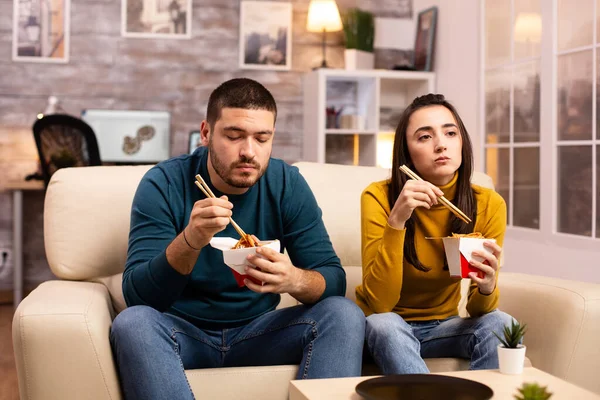 在现代舒适的客厅里，情侣们一边看电视一边吃着外卖面 — 图库照片
