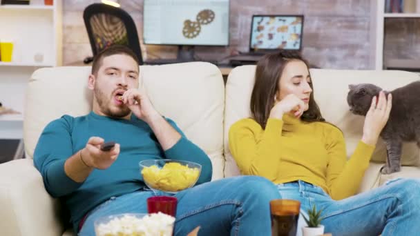 Homme barbu manger des puces et en utilisant la télécommande pour changer les chaînes de télévision — Video