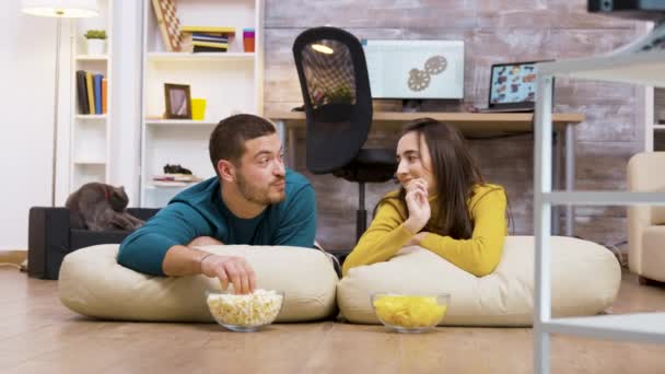 Веселая пара смотрит телевизор, сидя на подушках — стоковое видео