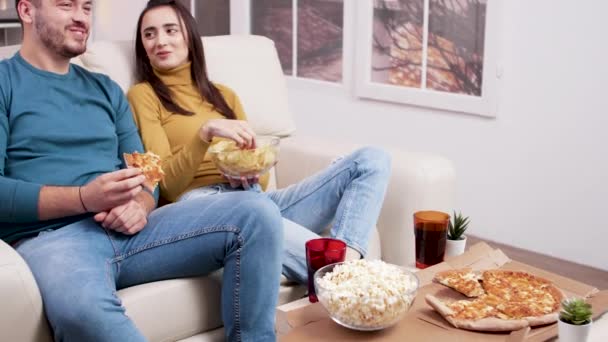 Кавказская молодая пара сидит на диване и ест пиццу — стоковое видео