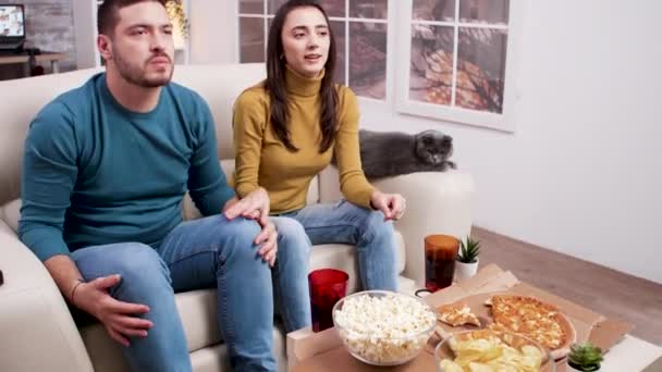 Zdenerwowana młoda para podczas oglądania meczu w telewizji — Wideo stockowe