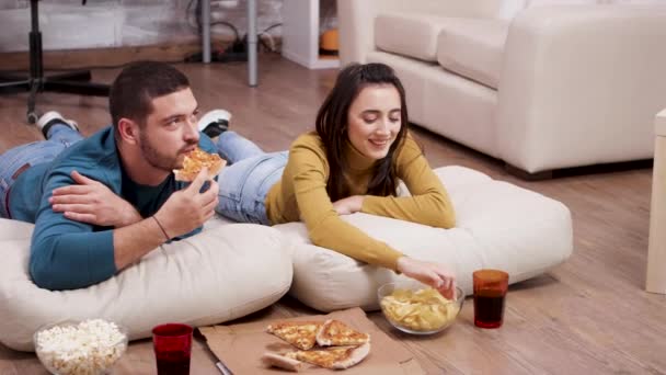 Relaxed couple sitting on the floor eating pizza and chips — Stockvideo