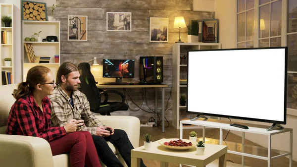 Веселая пара, сидящая на диване и играющая в видеоигры — стоковое фото