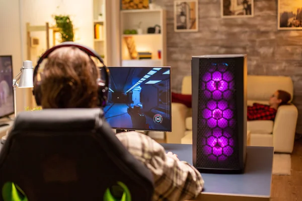 Visão traseira do jogador masculino jogando um atirador em seu computador PC poderoso tarde da noite na sala de estar — Fotografia de Stock