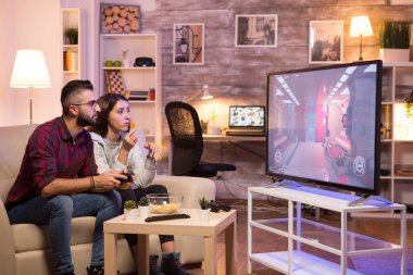 Adam kanepede oturuyor ve televizyonda video oyunları oynuyor.