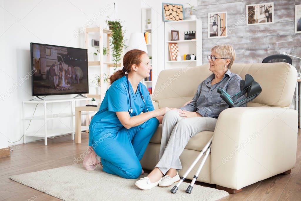 Nurse in knees talking with old woman
