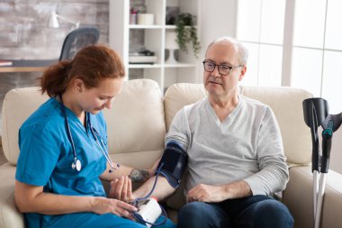 Kadın doktor yaşlı adamın tansiyonunu ölçüyor.