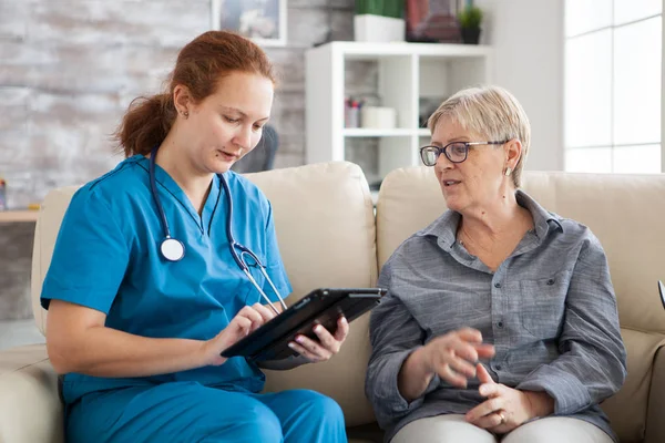 Senior woman and female nurse with tablet sitting on couch — 스톡 사진