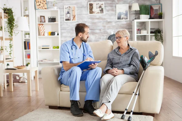 Male doctor with senior woman sitting on couch — Stock Photo, Image