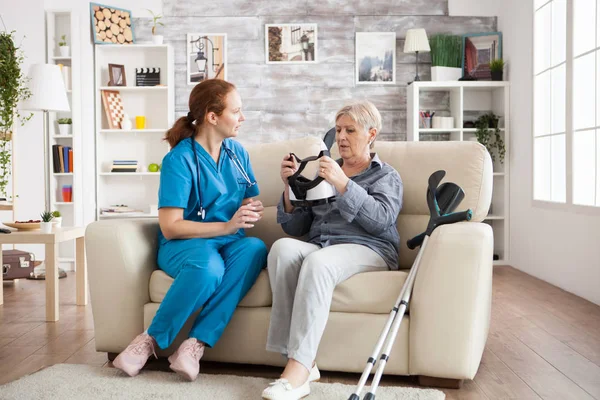 Mujer de edad avanzada sentada en el sofá con la enfermera —  Fotos de Stock