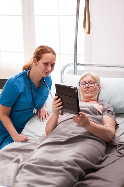 Ouderen leeftijd vrouw en vrouwelijke arts lezen op tablet computer — Stockfoto