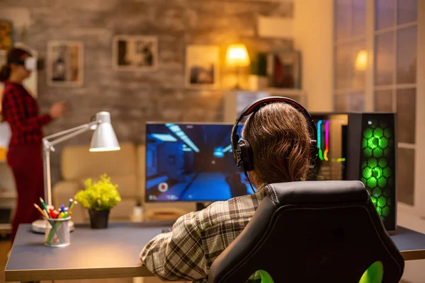 Vista trasera del videojuego profesional jugando en un PC potente tarde en la noche en la sala de estar —  Fotos de Stock