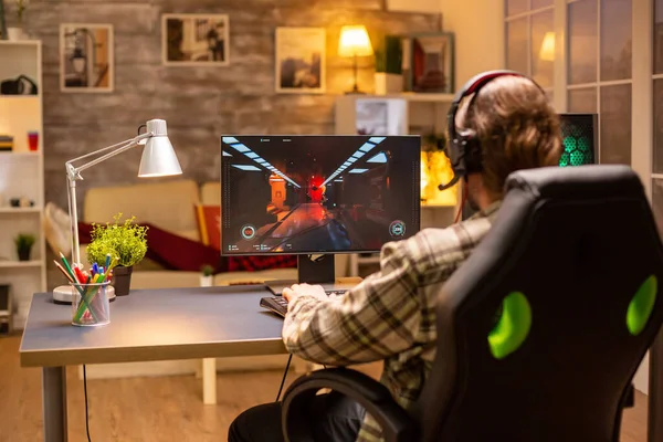 ライブルームで夜遅くに彼の強力なPCコンピュータ上でシューティングゲームをプレイゲーマー男性のバックビュー — ストック写真