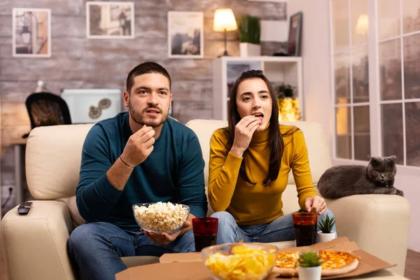 Belo jovem casal assistindo TV e comer fast food takeaway — Fotografia de Stock