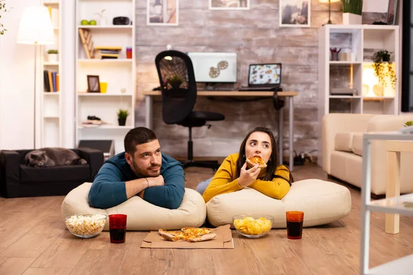 Casal sentado no chão e assistindo TV em sua sala de estar — Fotografia de Stock