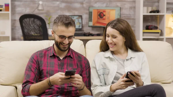 Casal rindo juntos enquanto navega em seus telefones — Fotografia de Stock