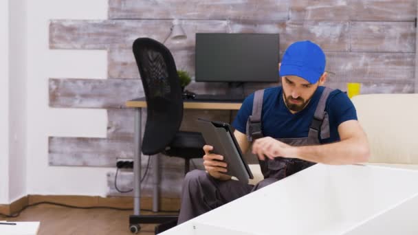 Männliche Arbeiter in Overalls mit einer Mütze, die Möbelmontage liest — Stockvideo