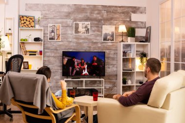 Oturma odasında TV seyreden bir çiftin arka görüntüsü.