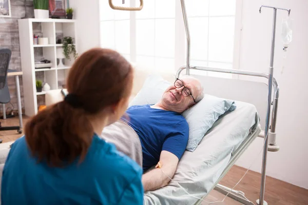 Vecchio in casa di cura sorridente al medico femminile — Foto Stock