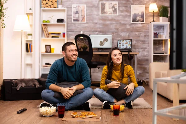 Pár sedí na podlaze a dívají se na televizi v obýváku — Stock fotografie