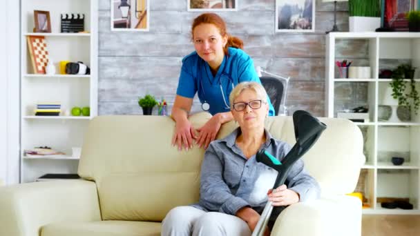 Vacker sjuksköterska på vårdhem och gammal kvinna sitter på soffan — Stockvideo