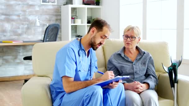 Orvosi asszisztens jegyzetel az írótáblán, miközben az öregasszonyt hallgatja az idősek otthonában. — Stock videók