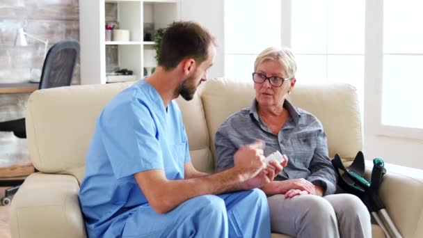 Помощник врача сидит на диване со старшей женщиной — стоковое видео