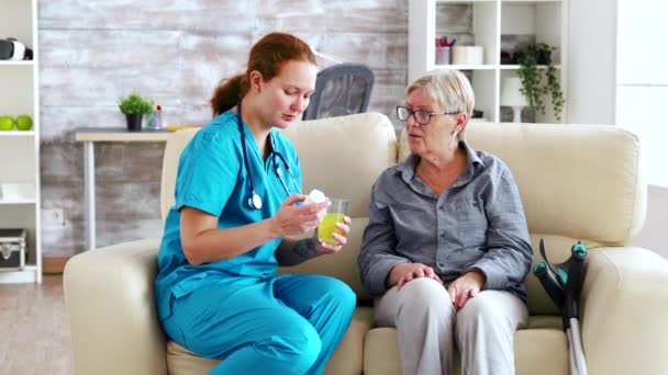 Medico femminile seduto sul divano con la donna anziana in casa di cura dando le sue pillole quotidiane — Video Stock