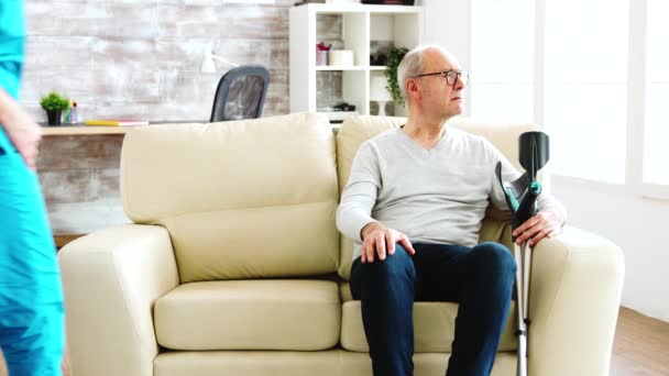 Infermiera donna che si prende cura di un vecchio paziente con malattia di Alzheimer seduto sul divano in casa di cura — Video Stock