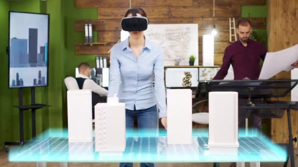 Arquitecta mujer con auriculares VR está mirando proyecciones holográficas de la construcción de una ciudad — Vídeos de Stock