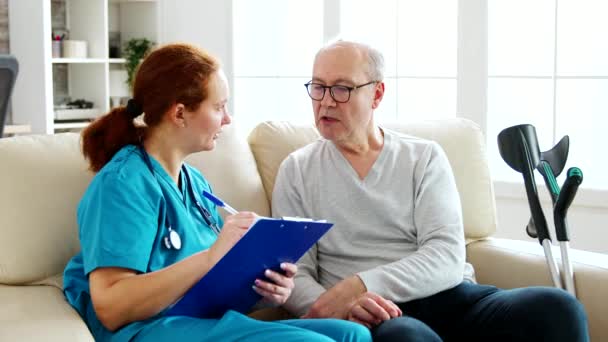 Assistante de santé féminine prenant des notes sur la santé d'un vieil homme dans une maison de retraite confortable — Video