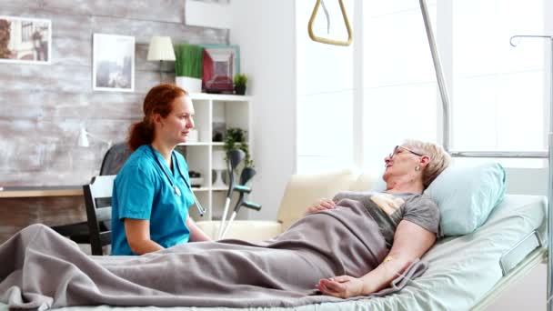 A nővér az öregek otthonában egy idős hölggyel beszél, aki a kórházi ágyban fekszik. — Stock videók
