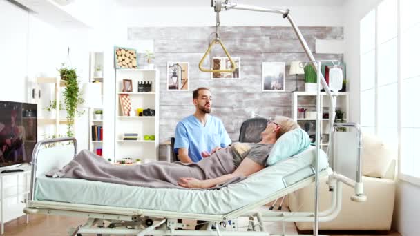 Cuidador en casa de retiro hablando con una anciana acostada en la cama del hospital — Vídeo de stock