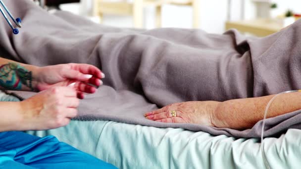 Foto ravvicinata di un giovane assitente caucasico che prende la mano di una vecchia signora sdraiata nel letto d'ospedale — Video Stock