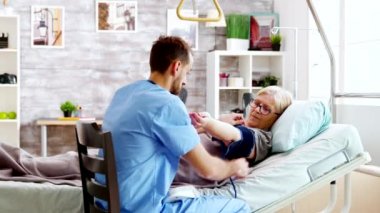 Huzurevinde erkek hemşire yaşlı kadının kan basıncını ölçüyor.