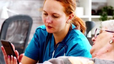 Hemşire, engelli bir kadının akıllı telefon kullanmasına yardım ederken yakın plan.