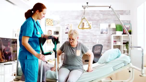 Assistente social ou enfermeira ajudando uma mulher idosa a andar com muletas — Vídeo de Stock