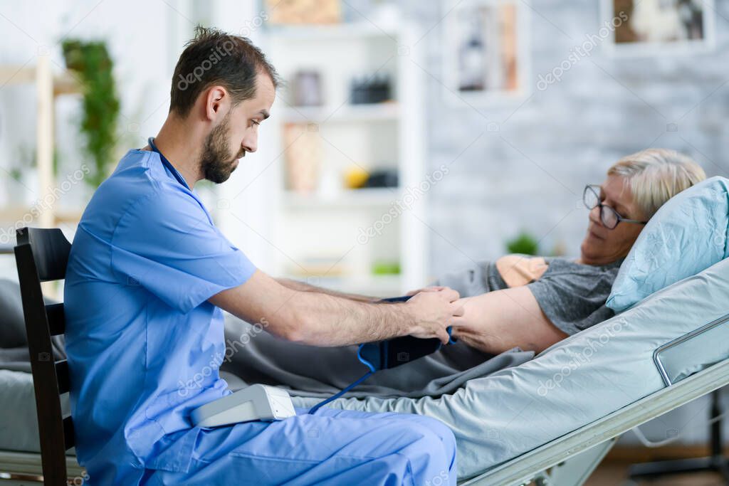 Bearded health visitor in a nursing home with stethoscope checking old lady