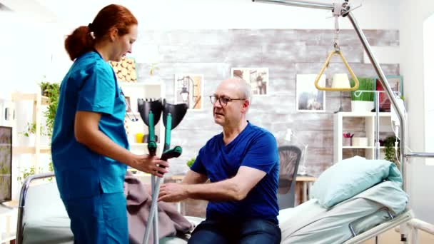 Nurse helping a disabled retired old man to stand up from his hospital bed — Stock Video