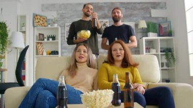 Genç kadınlar kanepede oturup televizyon izlerken gülümserler.