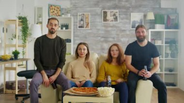 Bir grup arkadaş kanepede oturmuş pizza için uzanıyorlar.