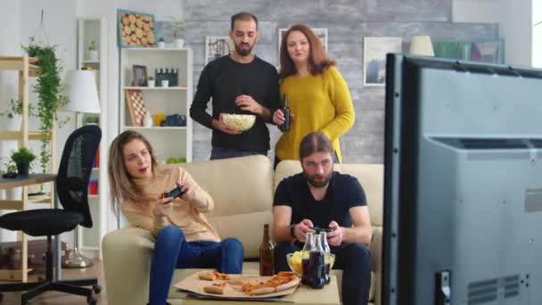 Νεαρό ζευγάρι τρώει ποπ κορν ενώ οι φίλοι τους παίζουν βιντεοπαιχνίδια — Αρχείο Βίντεο